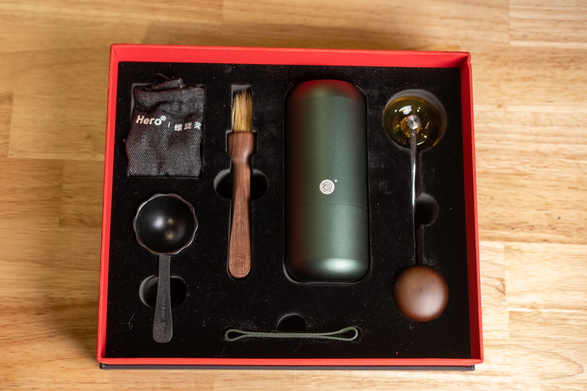 LAMOSE zeroHero manual coffee grinder Z7 kit in dark green with wood and metal accessories (scoop, brush, hopper) in a red gift box, overhead shot.