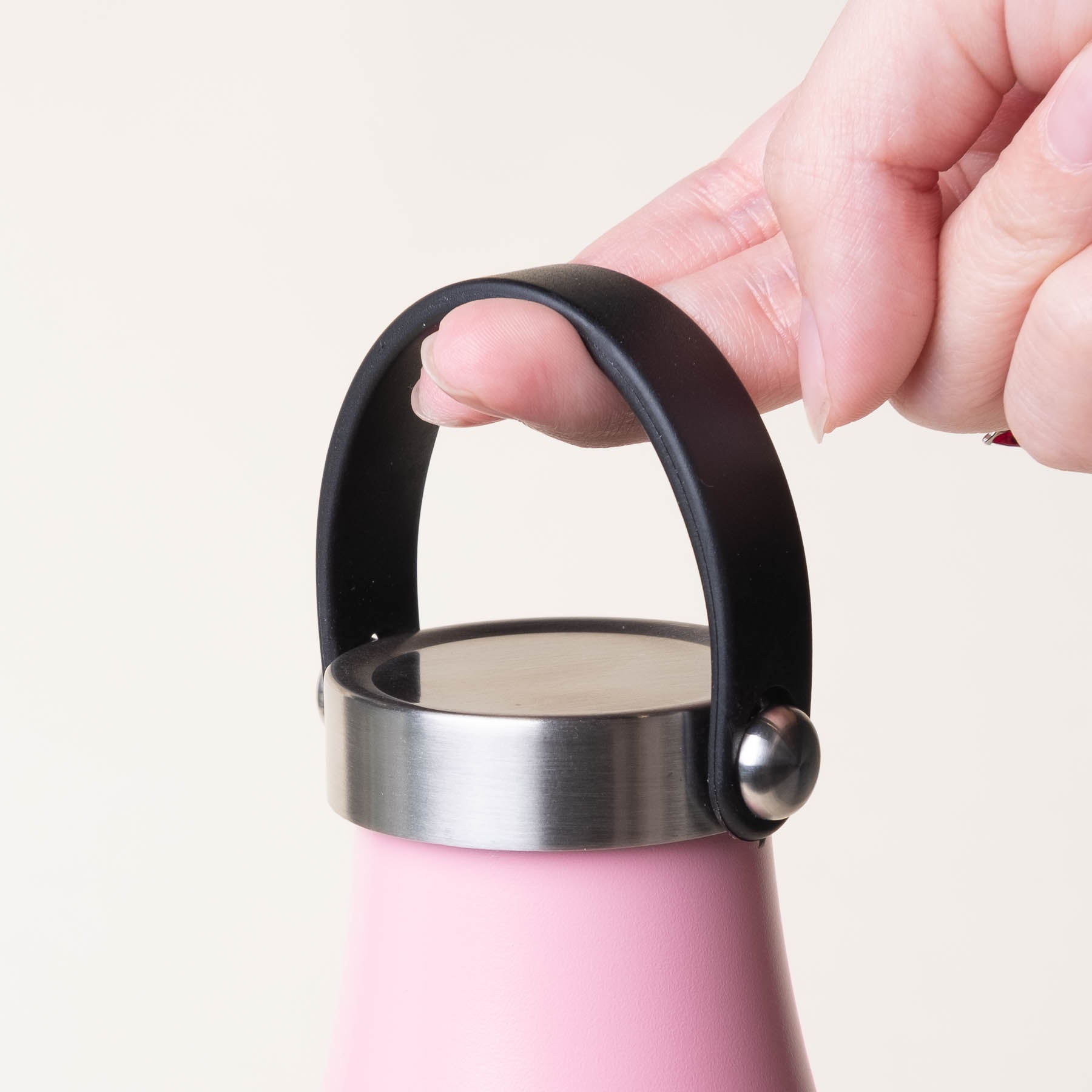 LAMOSE Robson Carry Lid, black silicone handle, brushed stainless steel top, held by hand on a pink bottle. Close-up, ergonomic design.