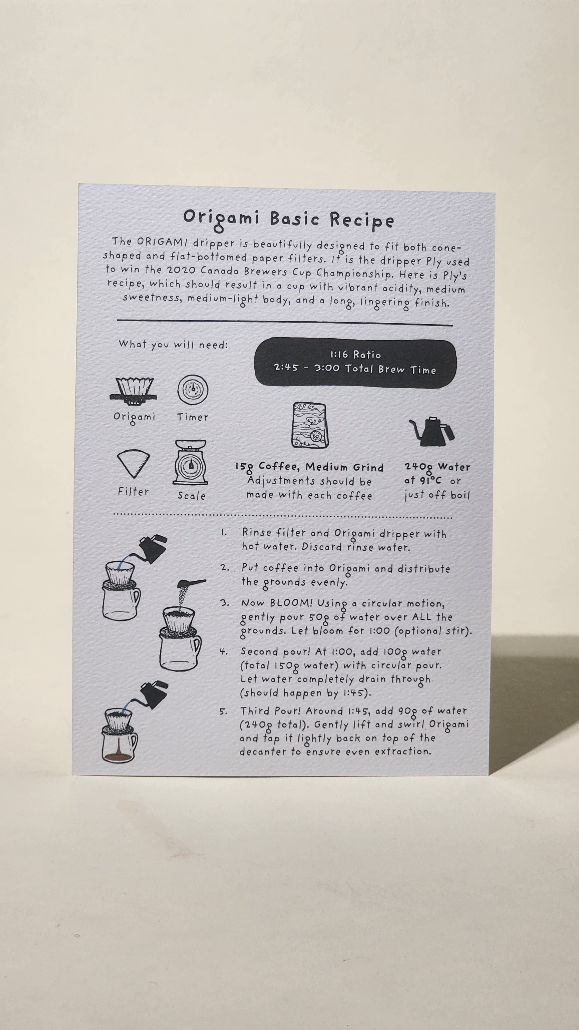 LAMOSE white Origami coffee brew guide recipe card on textured paper, flat lay. Features detailed steps, illustrations for tools & ingredients.