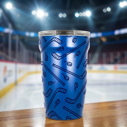 LAMOSE Peyto Pro Enamel 12oz tumbler in blue featuring a repeating pattern of dark blue hockey sticks and speeding pucks, set against a blurred hockey rink background.