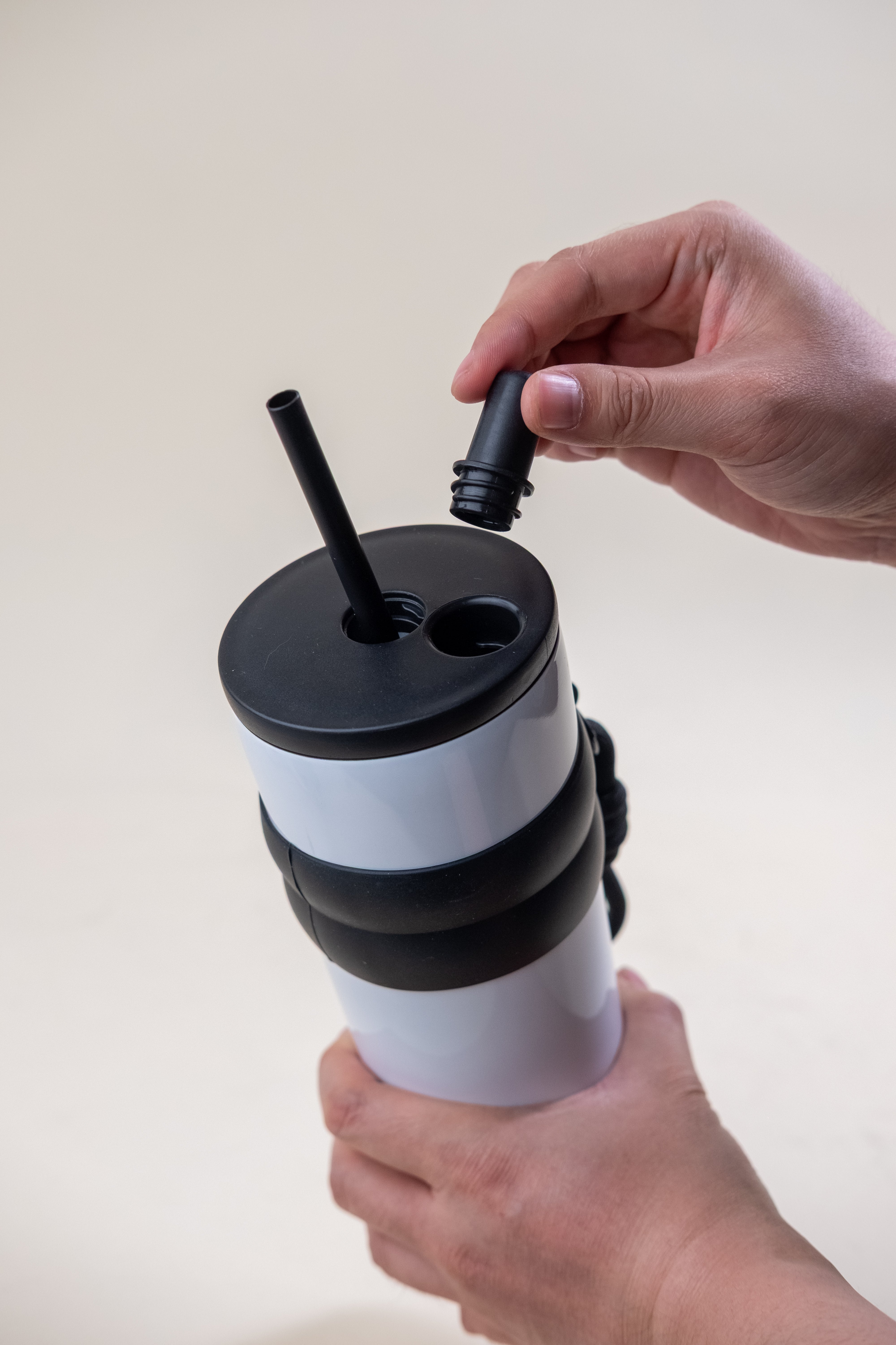 Close-up view of a person adjusting the lid on a white and black straw tumbler, showcasing the tumbler’s flexible design with multiple openings for enhanced drink access. 