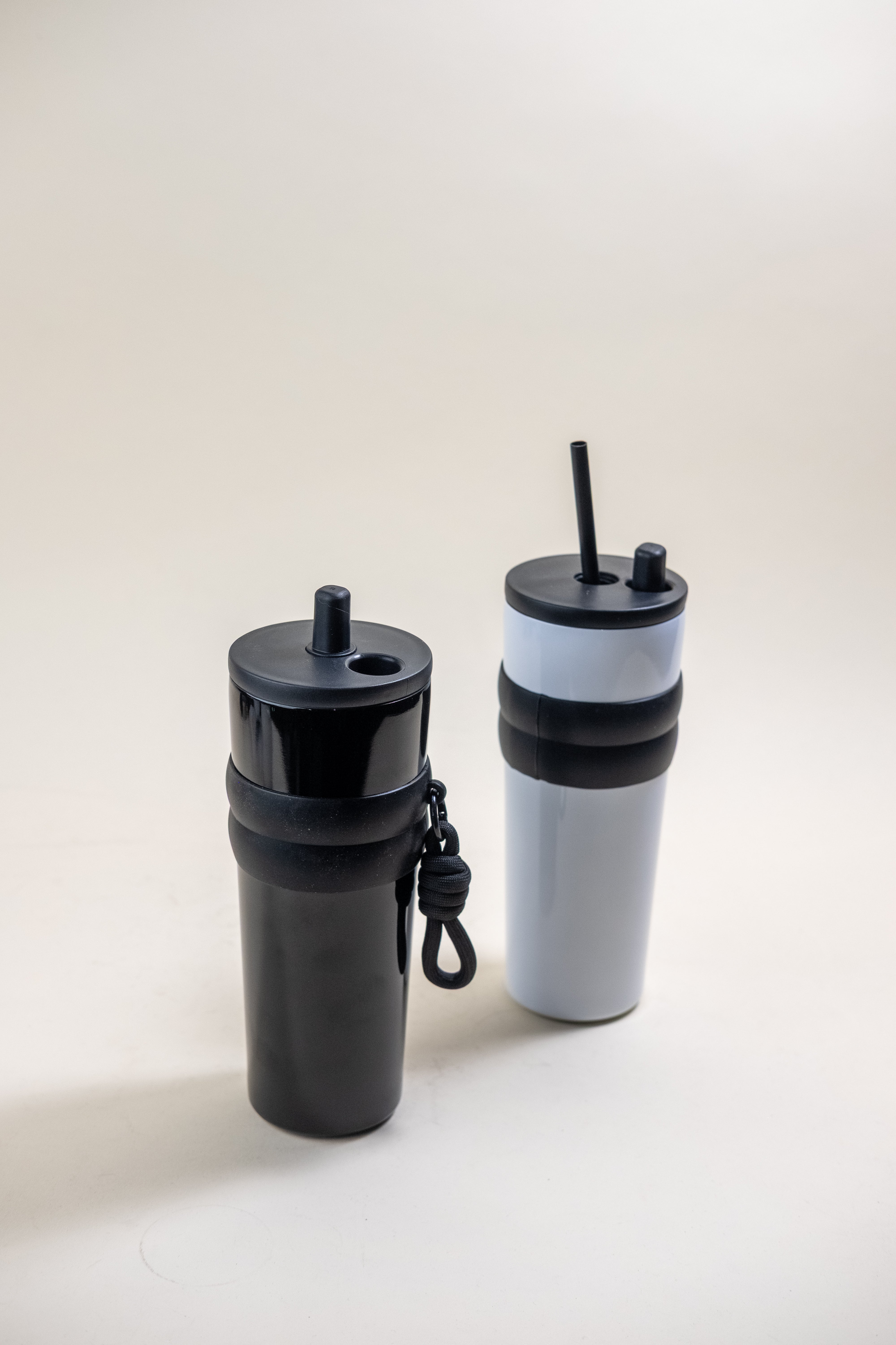 Two stainless steel straw tumblers, one in solid black and the other in white with black accents, both equipped with BPA-free plastic straws and rubber grips, showcasing their sleek design and ease of use. 