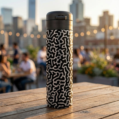 LAMOSE Emerald 16 oz stainless steel tumbler featuring a white and black organic maze pattern sitting on a wooden table on a rooftop.