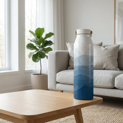 Grouse 34 oz insulated tumbler featuring a white body fading into a blue geometric triangle pattern sitting on a wooden table in a sunny minimalist living room.