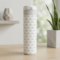 Close up of off-white Emerald 16 oz tumbler featuring a textured golf ball dimple pattern standing on a light wood surface.