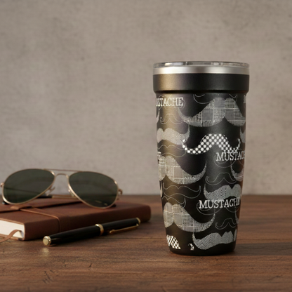 Black 16oz travel tumbler featuring white illustrated mustache patterns standing on a wooden desk next to gold sunglasses, a black pen, and a brown notebook.