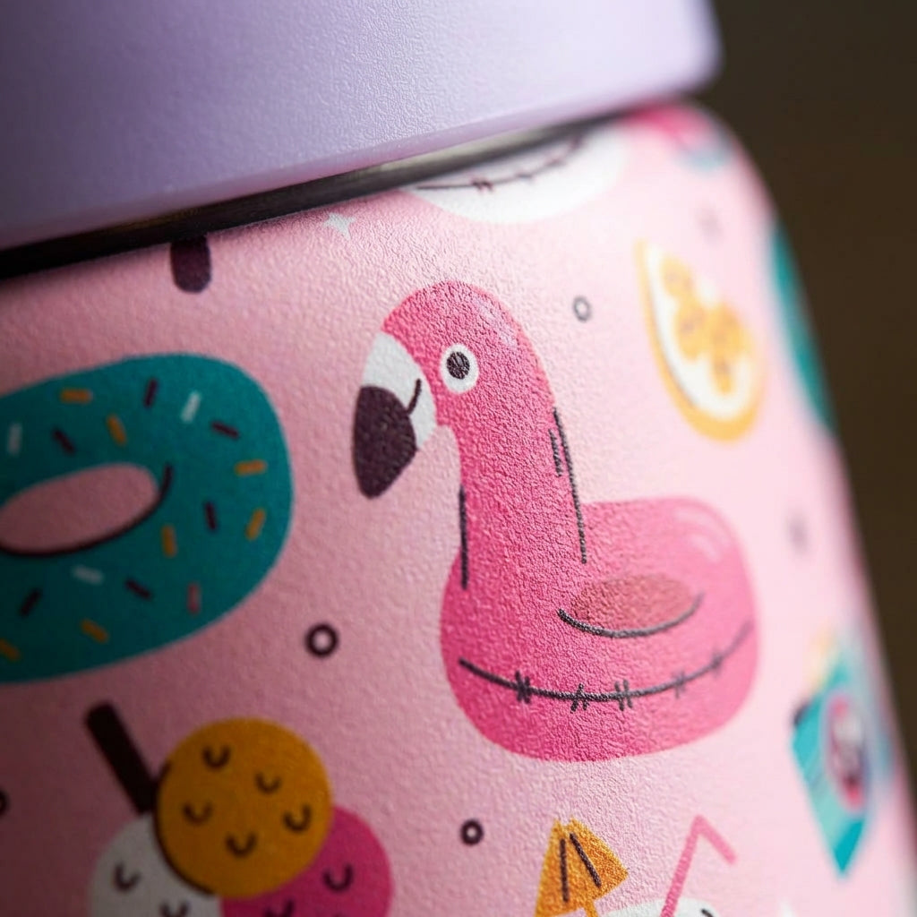 Detail shot - LAMOSE Goose 14oz kids water bottle featuring a pink body with flamingo floats, watermelon, and unicorn pattern, light purple lid and green handle, sitting poolside.