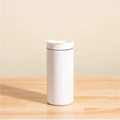 LAMOSE Grouse 12 oz travel tumbler in matte white, with a flip-open lid, shown from the front on a wooden surface.