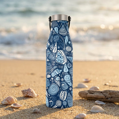 LAMOSE Robson 21 oz insulated water bottle in deep blue with white seashell and spiral patterns standing on a sandy beach next to driftwood.