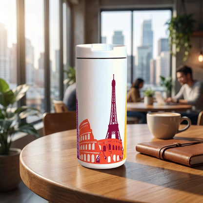White 12 oz insulated travel mug featuring colorful artistic illustrations of the Eiffel Tower and Colosseum sitting on a wooden cafe table.