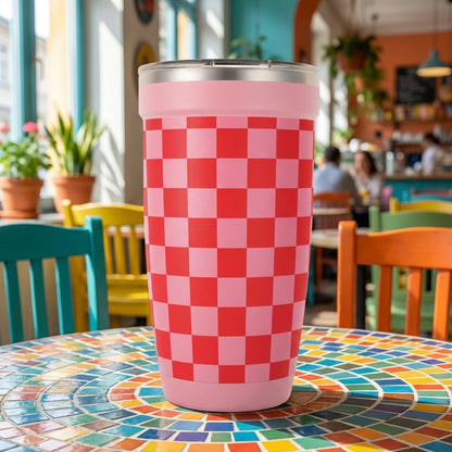 Peyto 16oz pink insulated tumbler with red and light pink checkerboard pattern sitting on a colorful mosaic cafe table.
