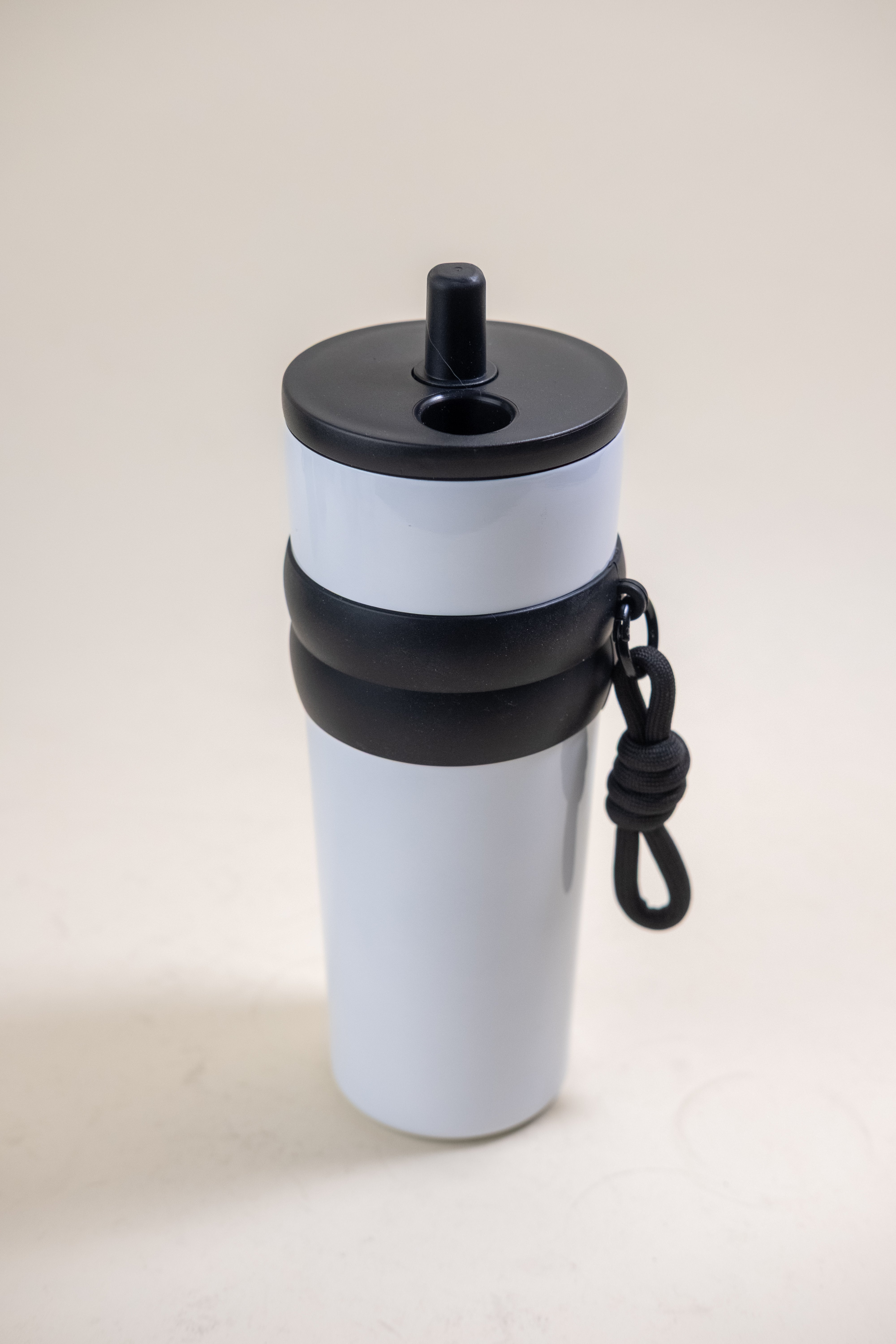 Elegant white and black stainless steel straw tumbler equipped with a BPA-free black plastic straw and a black rubber grip, complete with a practical carrying rope for easy transport. 