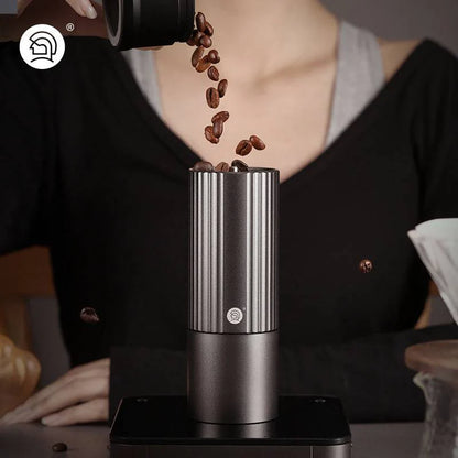 LAMOSE zeroHero Z3 Pro manual coffee grinder, dark grey stainless steel. Elevated front view, person pouring coffee beans into hopper.