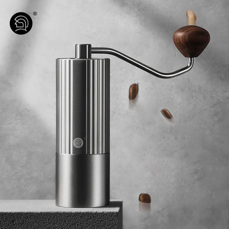 LAMOSE zeroHero Z3 Pro manual coffee grinder, sleek silver stainless steel with ribbed body, wooden handle, front view, falling coffee beans.