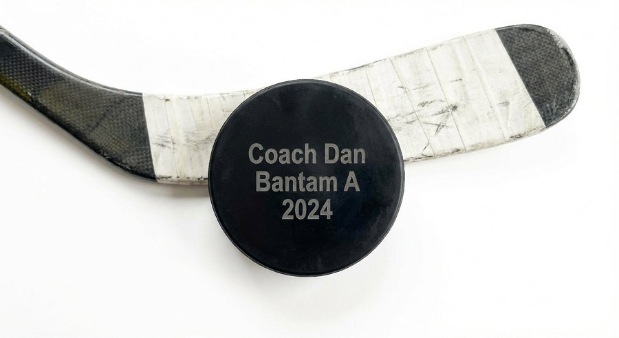 Overhead flat lay laser engraved coach puck with hockey stick on ice