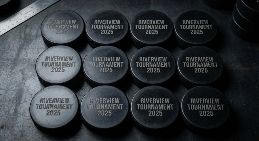 Overhead 12 black hockey pucks in grid Riverview Tournament 2025 engraved