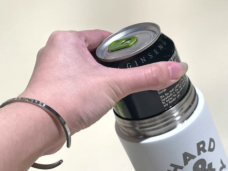 White LAMOSE Logan 16 oz insulated can cooler with 'HARD' text, holding a black Monster energy drink, held by hand with bracelet.