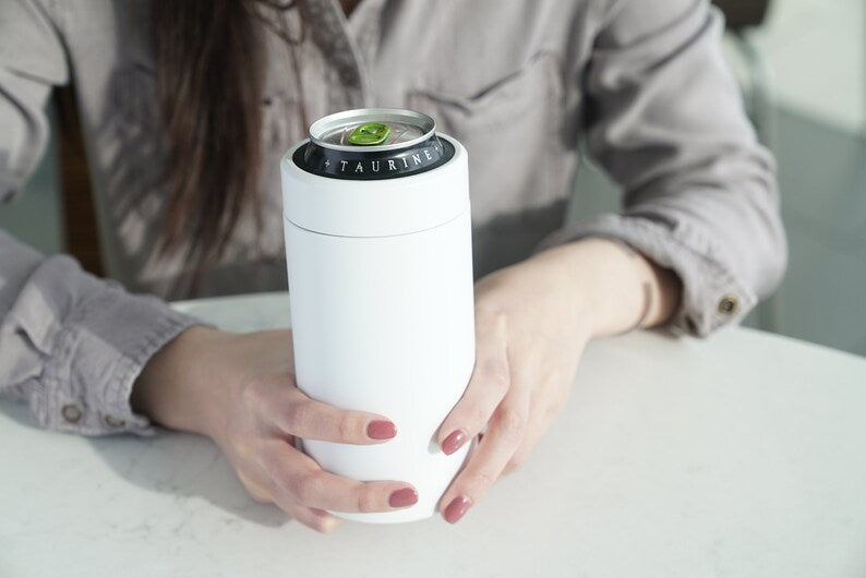 LAMOSE Logan 16 oz white stainless steel can cooler, front view, held by hands, with an open 'TAURINE' beverage can.