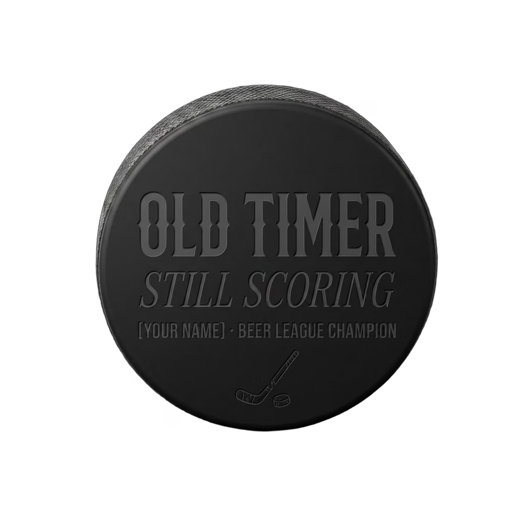 "Old Timer · Still Scoring" Beer League Hockey Puck — laser-engraved hockey puck, tonal black-on-black engraving on vulcanized rubber, made in Calgary