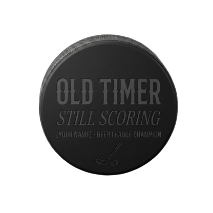 "Old Timer · Still Scoring" Beer League Hockey Puck — laser-engraved hockey puck, tonal black-on-black engraving on vulcanized rubber, made in Calgary