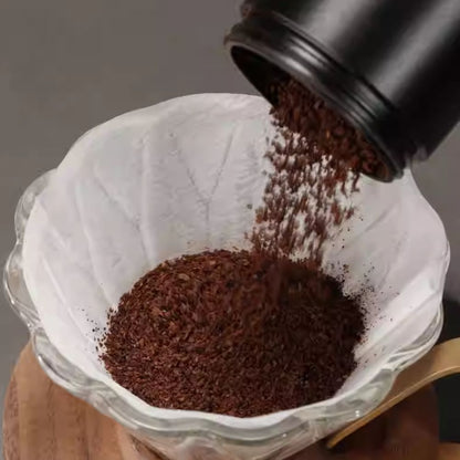 White LAMOSE zeroHero V01 pour-over paper filter in a glass dripper as coffee grounds are poured in. Top-down view.