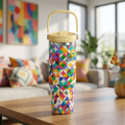 LAMOSE Cascade 40oz stainless steel tumbler featuring colorful geometric shapes and a yellow handle sitting on a wooden coffee table in a bright living room.